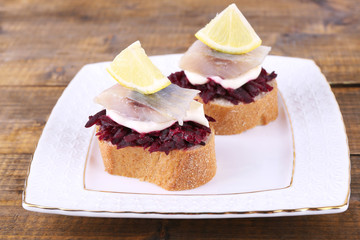 Rye toasts with herring and beets on plate on wooden background