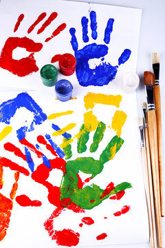 Hand prints of paint, paints and brushes on white background