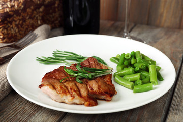 Steak with herbs on plate and bottle of wine on wooden table