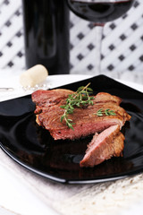 Steak with herbs on plate with wine on wooden background