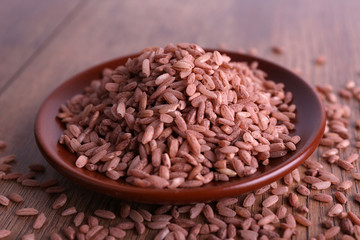 Red rice on plate on wooden background