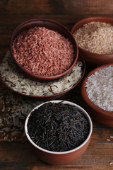 Different kinds of rice in bowls on wooden background