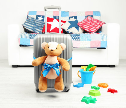 Suitcase with teddy bear and child toys in room