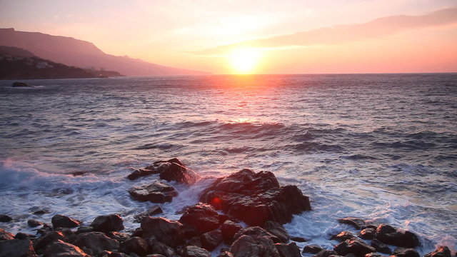 Waves break about stones at sunrise over the sea