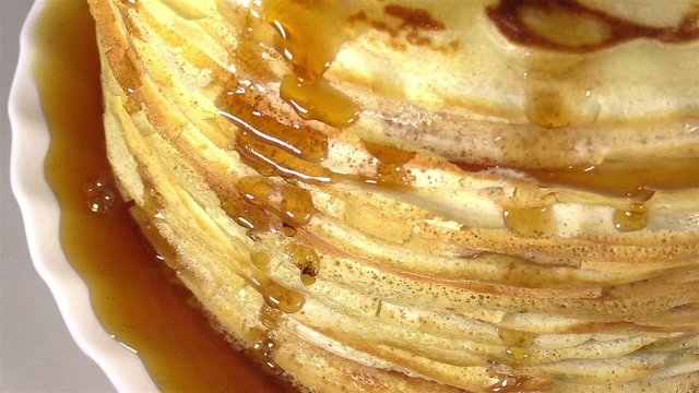 A stack of thin pancakes with honey