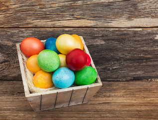 Colorful Easter eggs in basket on wooden background