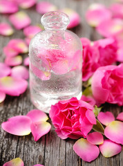 Essential oil with rose petals on wooden background
