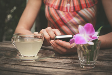 Young woman drinking tea and using her phone