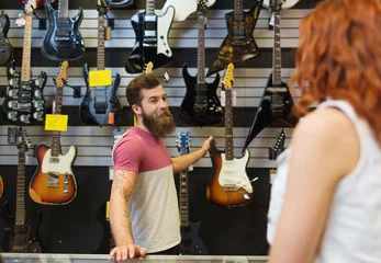 Keuken foto achterwand Muziekwinkel assistent die de gitaar van de klant laat zien in de muziekwinkel