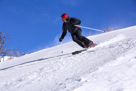 Skier with a mask on face skiing downhill in high mountains and sunny day