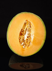 Cantaloupe melon fruit on black reflective surface isolated