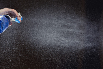 hand holding spray bottle and spraying on black background