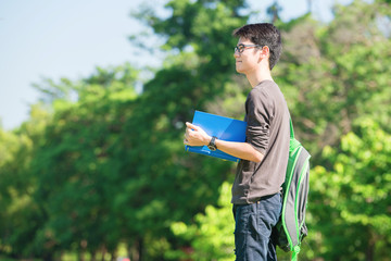 Asian student holding books and smiling while standing in park a