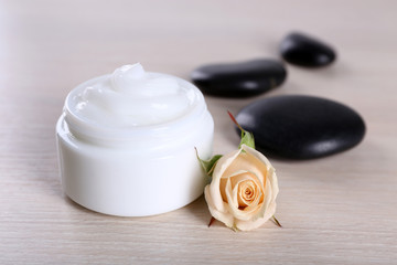Cosmetic cream with spa stones and rose on wooden background