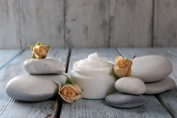 Cosmetic cream with flowers and spa stones on wooden background