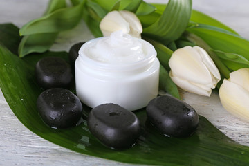 Cosmetic cream with flowers and spa stones on wooden background