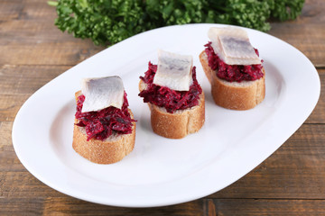 Rye toasts with herring and beets on plate on wooden background