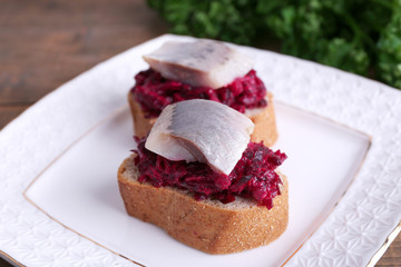 Rye toasts with herring and beets on plate on wooden background