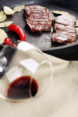 Glass of wine and steak in frying pan on table close up