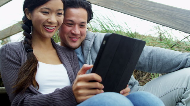 Laughing Ethnic Male Female Wireless Tablet Outdoors Beach 