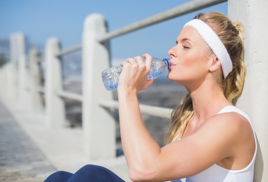 Fit blonde sitting on the pier drinking water