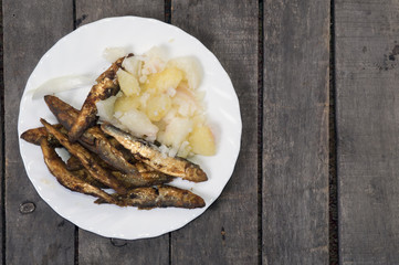 Fried smelts with potato salad on plate