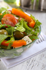 Greek salad in glass dish on napkin and color wooden background