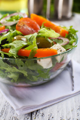 Greek salad in glass dish on napkin and color wooden background