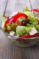 Greek salad in glass dish on wooden table background
