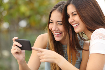 Women friends laughing and sharing media in a smart phone
