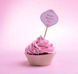 Delicious cupcake with inscription on table on pink background