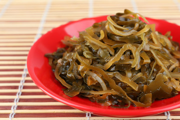 Seaweed in red bowl on bamboo mat background