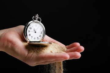 Silver pocket clock in hands and sand flowing away