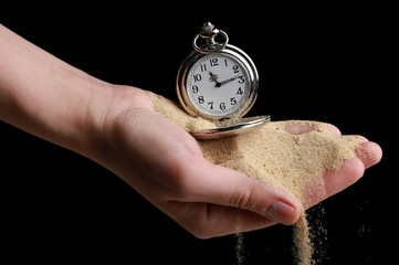 Silver pocket clock in hands and sand flowing away