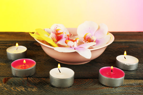 Bowl with orchids and candles on table on bright background