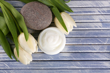 Cosmetic cream with flowers and spa stones on wooden background