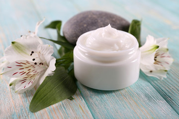 Cosmetic cream with flowers and spa stones on wooden background