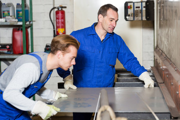 Two workers bending sheet metal with large machine