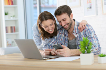 Couple at home using smartphone in front of laptop © goodluz