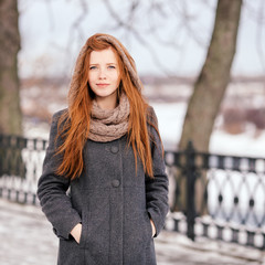 Beautiful redhead woman in grey coat strolling in winter park