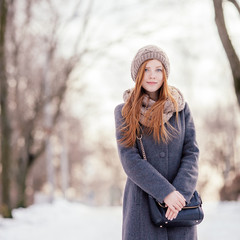 Beautiful redhead woman in grey coat strolling in winter park