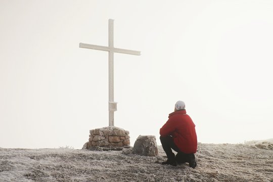 Tourist stand at cross of memorial on mountain peak  in Alps.