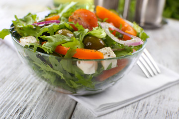 Greek salad in glass dish on napkin and color wooden background