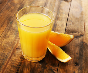 Glass of orange juice with slices on wooden table background
