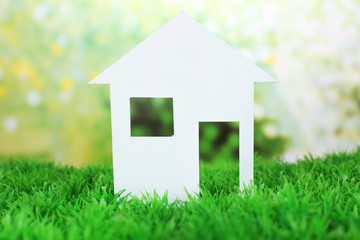 Cutout paper house on green grass and bright blurred background