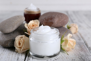 Cosmetic cream with flowers and spa stones on wooden background
