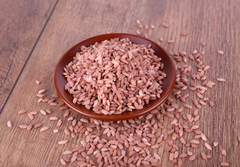 Red rice on plate on wooden background