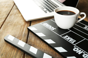 Movie clapper with laptop and cup of coffee on wooden