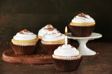 Delicious cupcakes with candle on table on brown background