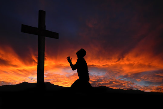 Silhouette of man praying to a cross with heavenly cloudscape su